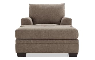 Brown fabric upholstered armchair with wide cushioned seat, padded arms, and supportive backrest, featuring dark wooden block legs.