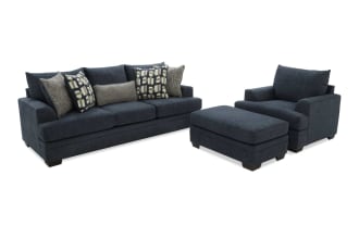 Dark blue fabric sofa set with three seat cushions, matching ottoman, and patterned throw pillows, modern living room furniture.