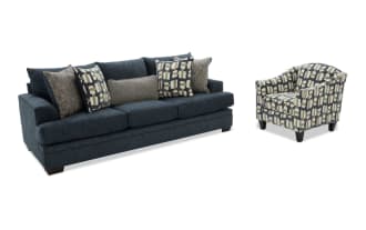 Dark blue fabric sofa with plush cushions and patterned throw pillows, paired with a modern armchair featuring a geometric multicolor fabric design and dark wooden legs.
