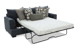 Dark gray fabric sofa bed with metal frame pull-out mattress, featuring six decorative patterned and textured throw pillows for added comfort and style.
