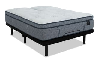 Mattress labeled "ENVY WELCOME TO BED" with a thick, quilted, gray fabric and white top, placed on a black metal bed frame with sturdy legs.
