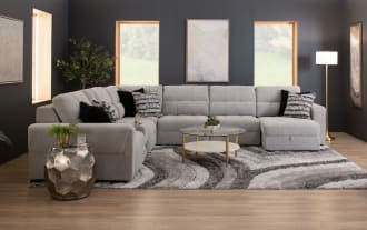 Light gray fabric sectional sofa with tufted cushions, L-shaped design, black and patterned throw pillows, and low black legs.