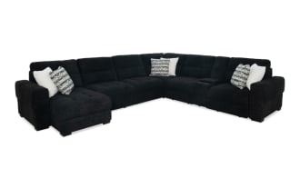 Large black fabric sectional sofa with plush cushions, L-shaped design, and decorative white and patterned throw pillows, ideal for modern living rooms.