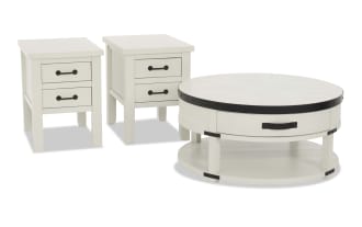Set of white wooden furniture including two square side tables with black metal handles and one round coffee table with a black metal rim and lower shelf, featuring a rustic farmhouse style.