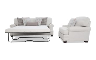 Beige fabric sleeper sofa with floral and plaid throw pillows, nailhead trim, and dark wooden legs, shown with mattress extended and side view.