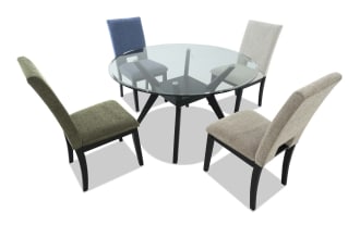 Round glass dining table with black wooden legs, accompanied by four upholstered chairs in blue, beige, light gray, and olive green fabric.
