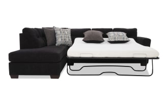 Black sectional sofa with a pull-out metal frame bed, white mattress, and four decorative pillows in gray and patterned fabric, ideal for space-saving guest accommodations.