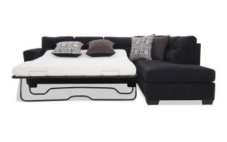 Black fabric sectional sofa with a pull-out metal frame sleeper bed, white mattress, and four decorative pillows in patterned and solid dark tones.