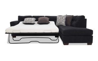 Black fabric sectional sofa with a pull-out metal frame bed mattress and four decorative pillows, combining seating and sleeping functionality.
