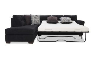 Black fabric sectional sofa with a pull-out metal frame sleeper bed, white mattress, and four decorative pillows in patterned and solid colors.