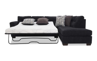 Black sectional sleeper sofa with a pull-out metal frame bed, white mattress, and four decorative pillows in patterned and solid dark fabric, designed for space-saving and multifunctional living rooms.