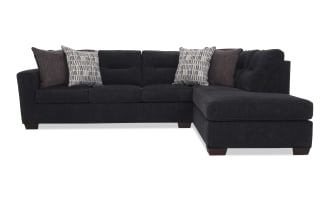 Dark gray sectional sofa with tufted back cushions, fabric upholstery, and decorative patterned and solid throw pillows, modern style.