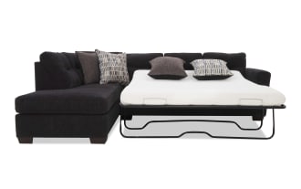 Black fabric sectional sofa with a pull-out bed mattress, featuring tufted cushions and patterned throw pillows, ideal for small living spaces.