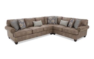 Brown leather sectional sofa with rolled arms, dark wooden legs, and multiple decorative patterned throw pillows, designed for living room seating.