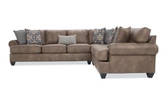 Brown leather sectional sofa with rolled arms, dark wooden legs, and multiple decorative patterned throw pillows, designed for living room seating.