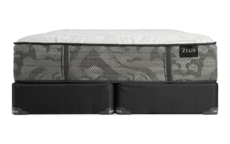 Zeus brand mattress with a gray patterned fabric side and white quilted top, resting on a black supportive base.
