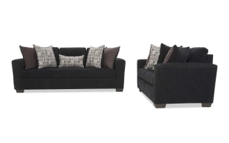 Dark charcoal fabric sofa with three seat cushions, flared arms, and six decorative pillows in patterned and solid brown tones, shown from front and side angles.