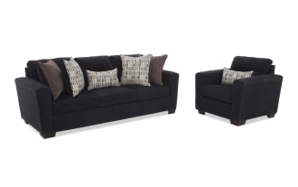 Dark gray fabric sofa with three seat cushions and five decorative pillows in patterned and solid brown shades, featuring wide armrests and wooden legs.
