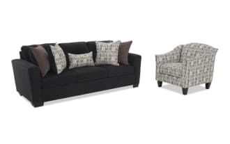 Dark gray fabric sofa with three seat cushions and five decorative pillows in patterned and solid brown tones, paired with a matching patterned fabric armchair with dark wooden legs.