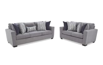 Modern gray fabric sofa with three seat cushions and multiple decorative throw pillows in blue and patterned designs, featuring dark wooden legs and a boxy armrest style.