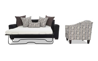 Black fabric sofa bed with metal frame, extended mattress, and multiple patterned and solid brown throw pillows; next to a patterned fabric armchair with wooden legs.