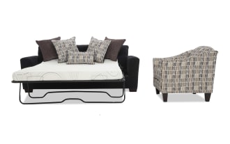 Black fabric sofa bed with metal frame mattress support, white mattress, and multiple decorative pillows; next to a patterned beige and brown upholstered armchair with wooden legs.