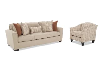 Beige fabric sofa with dark wooden legs, featuring three seat cushions and five decorative pillows in brown and patterned beige tones, paired with a matching patterned beige armchair with dark wooden legs.