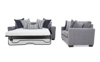 Gray fabric sofa bed with metal frame mattress support, featuring multiple patterned and solid blue throw pillows, shown from front and side angles.