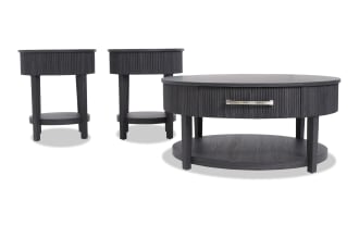 Set of three black wooden tables including one round coffee table with drawer and two matching round side tables, featuring ribbed texture and lower shelves.