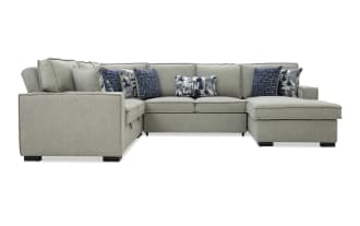 Gray fabric sectional sofa with chaise lounge, featuring multiple blue and patterned throw pillows, modern design with clean lines and black legs.