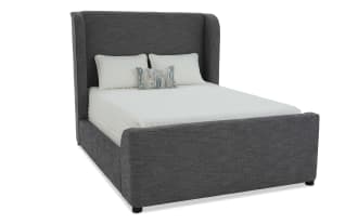 Modern upholstered bed frame in dark gray fabric with tall wingback headboard, white bedding, and decorative pillows for bedroom decor.