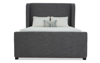 Modern upholstered bed frame in dark gray fabric with tall wingback headboard, white bedding, and decorative pillows for bedroom decor.