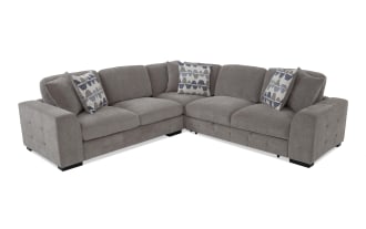 Gray fabric sectional sofa with tufted armrests, plush cushions, and geometric patterned throw pillows, designed for modern living rooms.