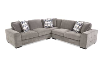 Gray fabric sectional sofa with tufted armrests, plush cushions, and three patterned blue and white throw pillows, ideal for modern living rooms.