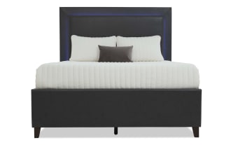 Modern black upholstered bed with padded headboard, white quilted bedding, and three pillows, featuring a sleek, minimalist design.