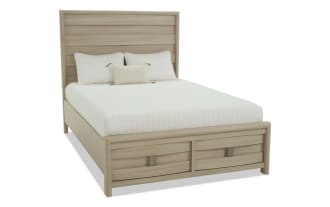 King-size wooden bed frame with light oak finish, featuring a paneled headboard and two front storage drawers, styled with white bedding and pillows.