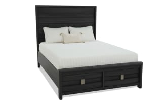 King-size bed with black wood frame, horizontal panel headboard, and two storage drawers at the footboard, styled with white bedding and pillows.