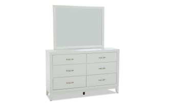 White wooden dresser with six drawers and silver handles, topped with a large rectangular mirror, modern minimalist bedroom furniture.
