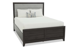 Twin bed with dark wood frame and upholstered gray fabric headboard, featuring white bedding and decorative pillows, modern style.