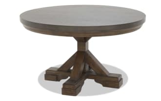 Round wooden dining table with dark brown finish, thick pedestal base with cross supports, rustic farmhouse style.