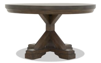 Round wooden dining table with dark brown finish, thick pedestal base with cross supports, rustic farmhouse style.