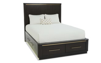 Dark wood bedroom set with a dresser and mirror, three-drawer nightstand with brass lamp, and a bed featuring storage drawers and brass accents.