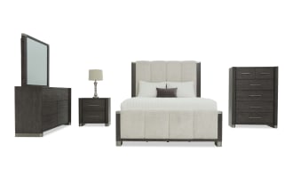 Modern bedroom furniture set featuring a dark wood finish with metal accents, including a tufted upholstered bed with cream fabric, matching dresser with mirror, nightstand with lamp, and tall chest of drawers.