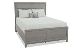 Gray wooden bed frame with a paneled headboard and footboard, styled with white bedding and decorative pillows, showcasing modern bedroom furniture.