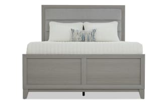 Gray wooden bed frame with a paneled headboard and footboard, styled with white bedding and decorative pillows, showcasing modern bedroom furniture.