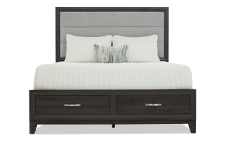 King-size bed with dark wood frame featuring two front storage drawers, a tall gray upholstered headboard, and white bedding with accent pillows.