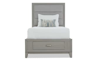 Gray wooden bedroom set with upholstered headboard, white bedding, matching dresser with mirror, and nightstand with lamp, modern style.