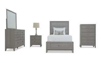 Gray wood bedroom set with upholstered headboard, including a dresser with mirror, nightstand with lamp, bed with storage drawer, and tall chest of drawers.