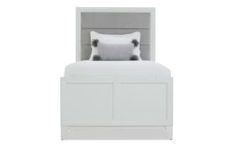 White bedroom furniture set featuring a twin bed with gray upholstered headboard, white wooden frame, matching dresser with mirror, nightstand with lamp, and tall chest of drawers.