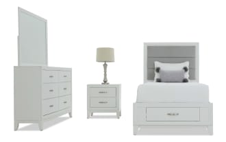 White bedroom furniture set including a dresser with mirror, nightstand with lamp, and twin bed with grey upholstered headboard and storage drawer.